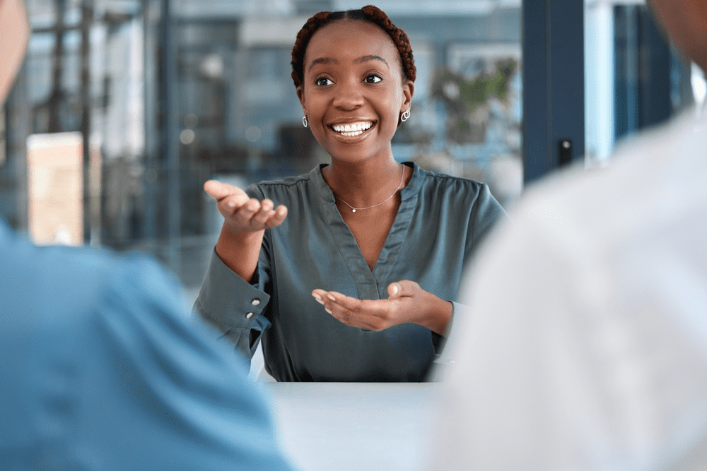 Mulher sorridente em uma conversa em ambiente de escritório, usando blusa cinza, praticando comunicação e liderança.