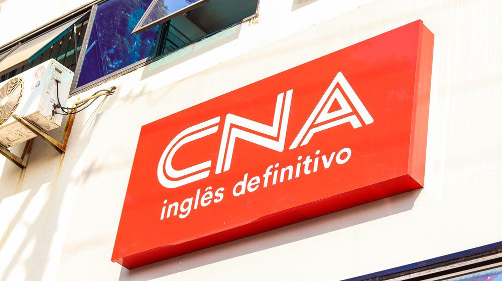 Placa de fachada de uma escola de inglês CNA destacando o curso de inglês definitivo, com foco na marca reconhecida e na metodologia de ensino de idiomas.